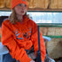 Person wearing All Day Fire Outfitters Deer Camp Hoodie outdoors by the campfire, showcasing warm and durable hunting and camping gear.