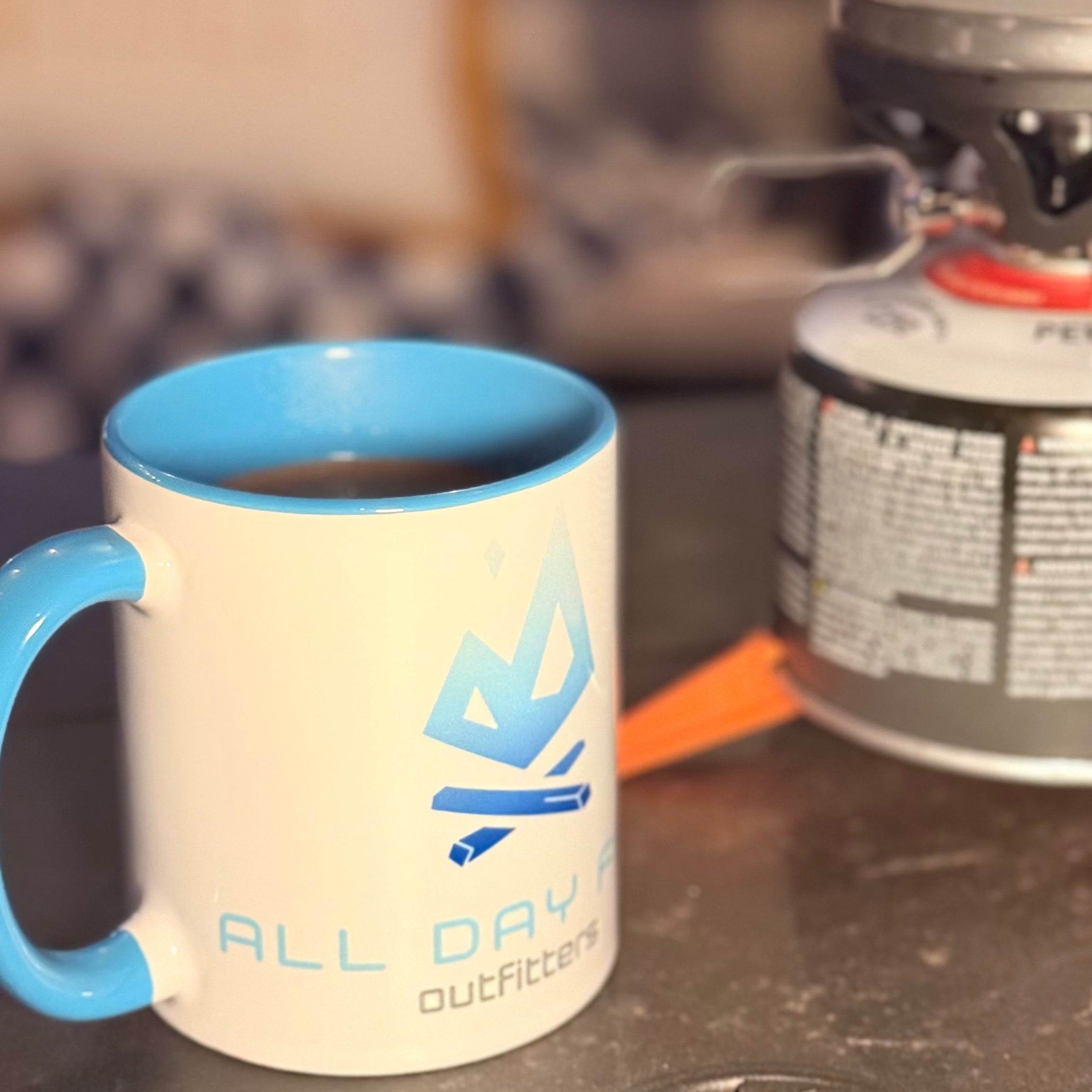 White mug with cambridge blue handle and All Day Fire Outfitters logo. Ceramic coffee mug for camping and outdoor use.