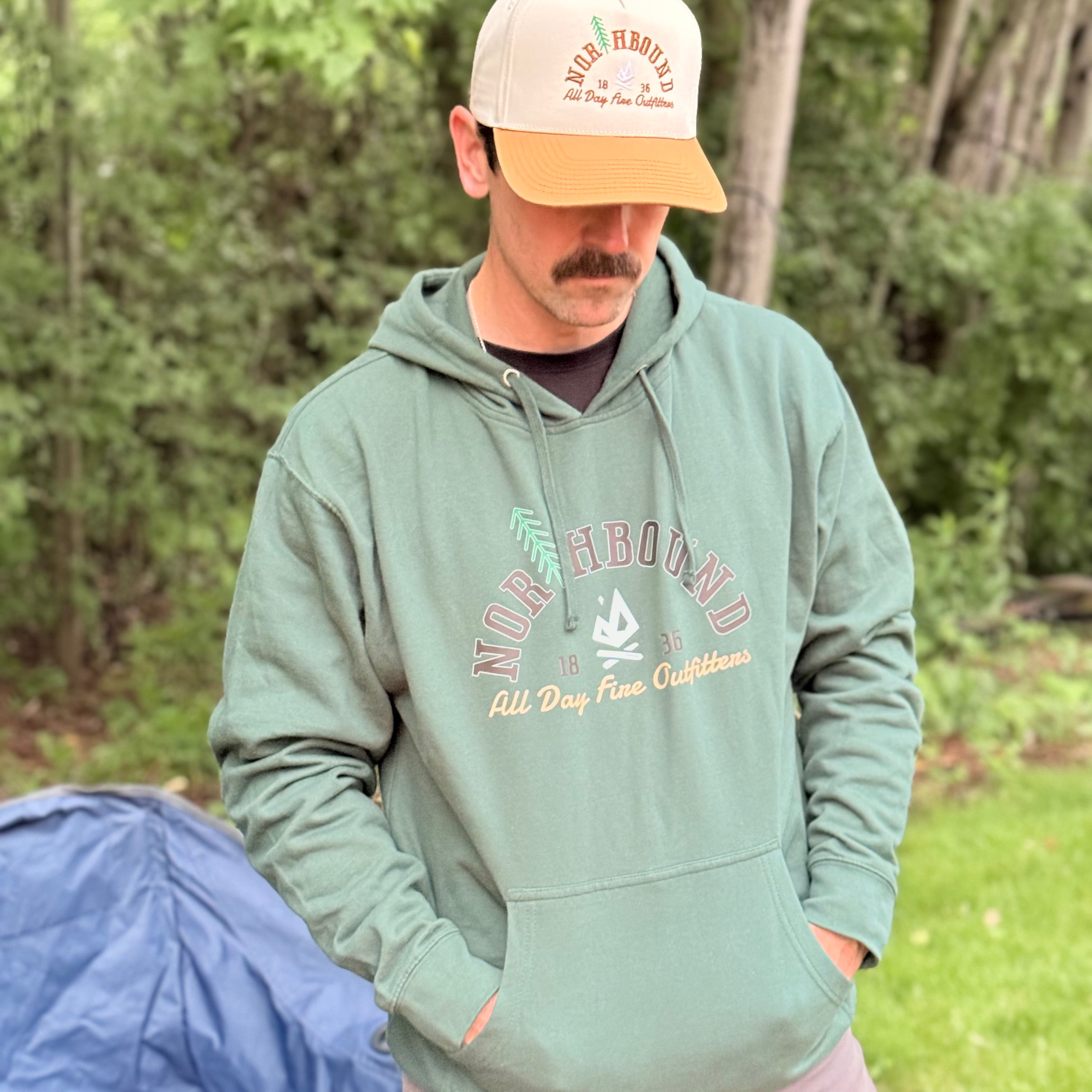 Man wearing the Northbound hoodie by All Day Fire Outfitters outdoors at a campsite, featuring embroidered-inspired Northbound artwork and Michigan Up North styling