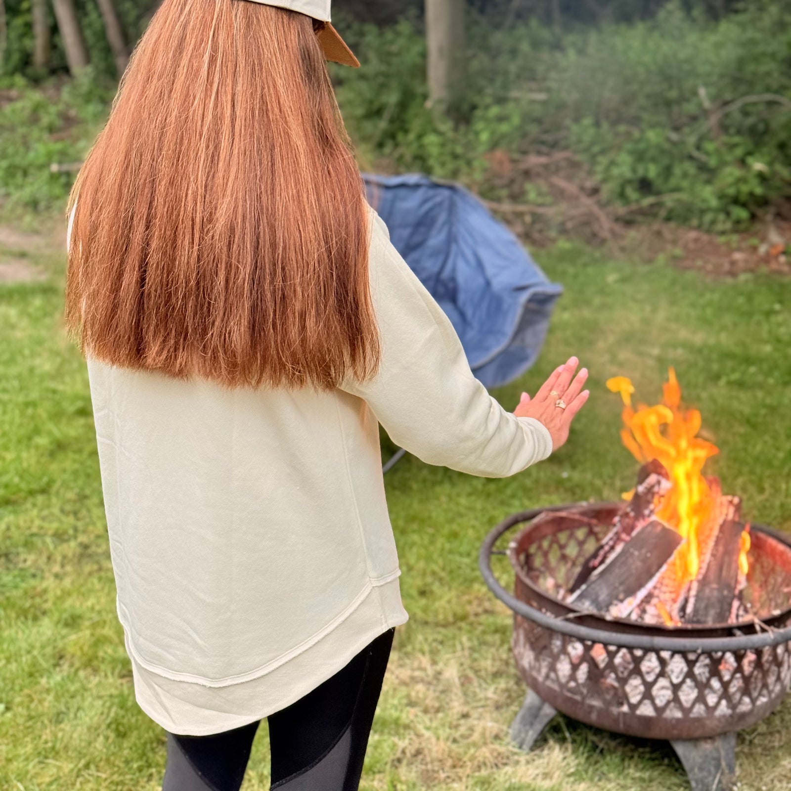 Woman gathered around a campfire wearing the Northbound women's crewneck inspired by Michigan Up North adventures.