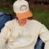 Woman wearing the Northbound women's crewneck and Northbound snapback hat while relaxing beside a campfire