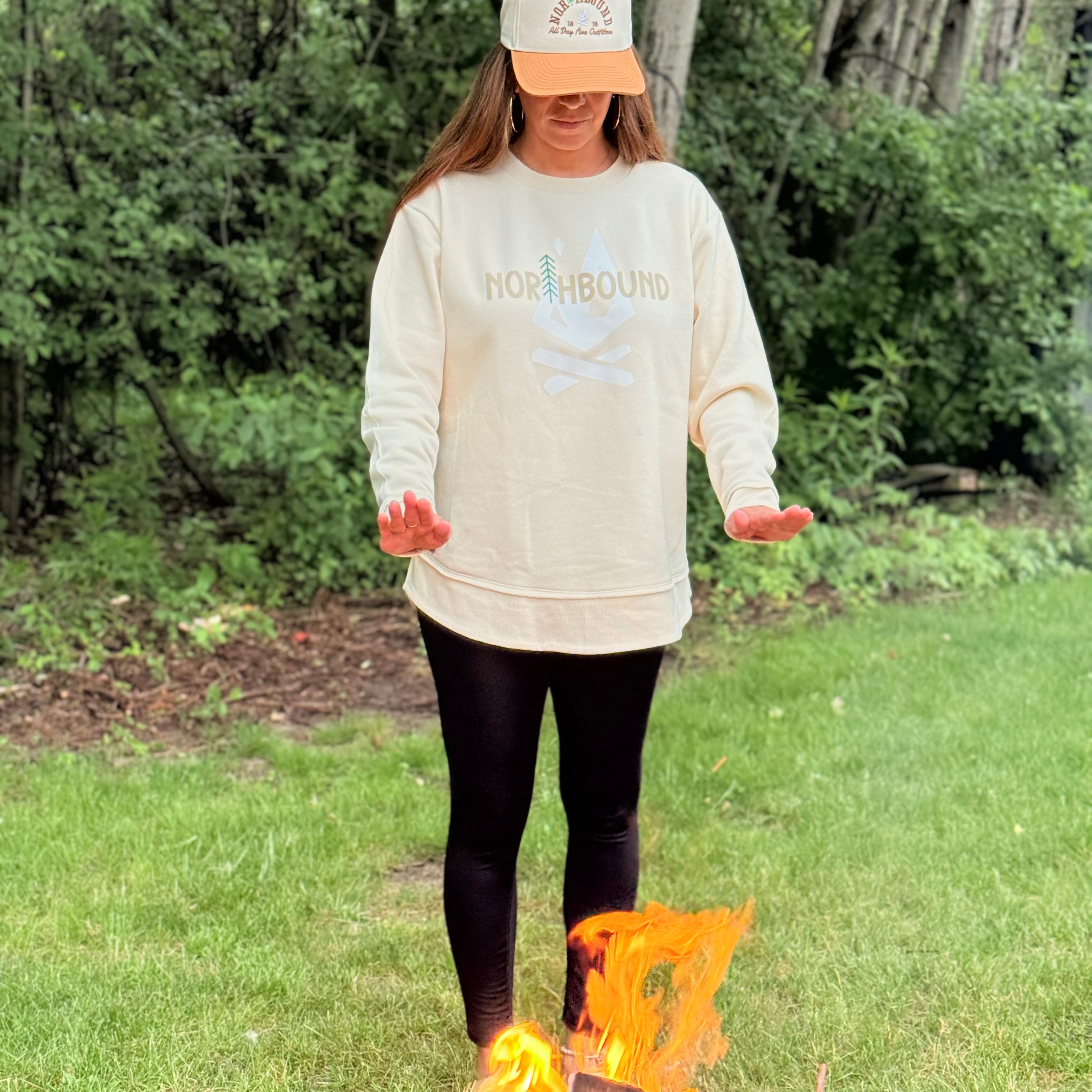 Woman wearing the Northbound women's crewneck and embroidered Northbound hat outdoors at a campsite.