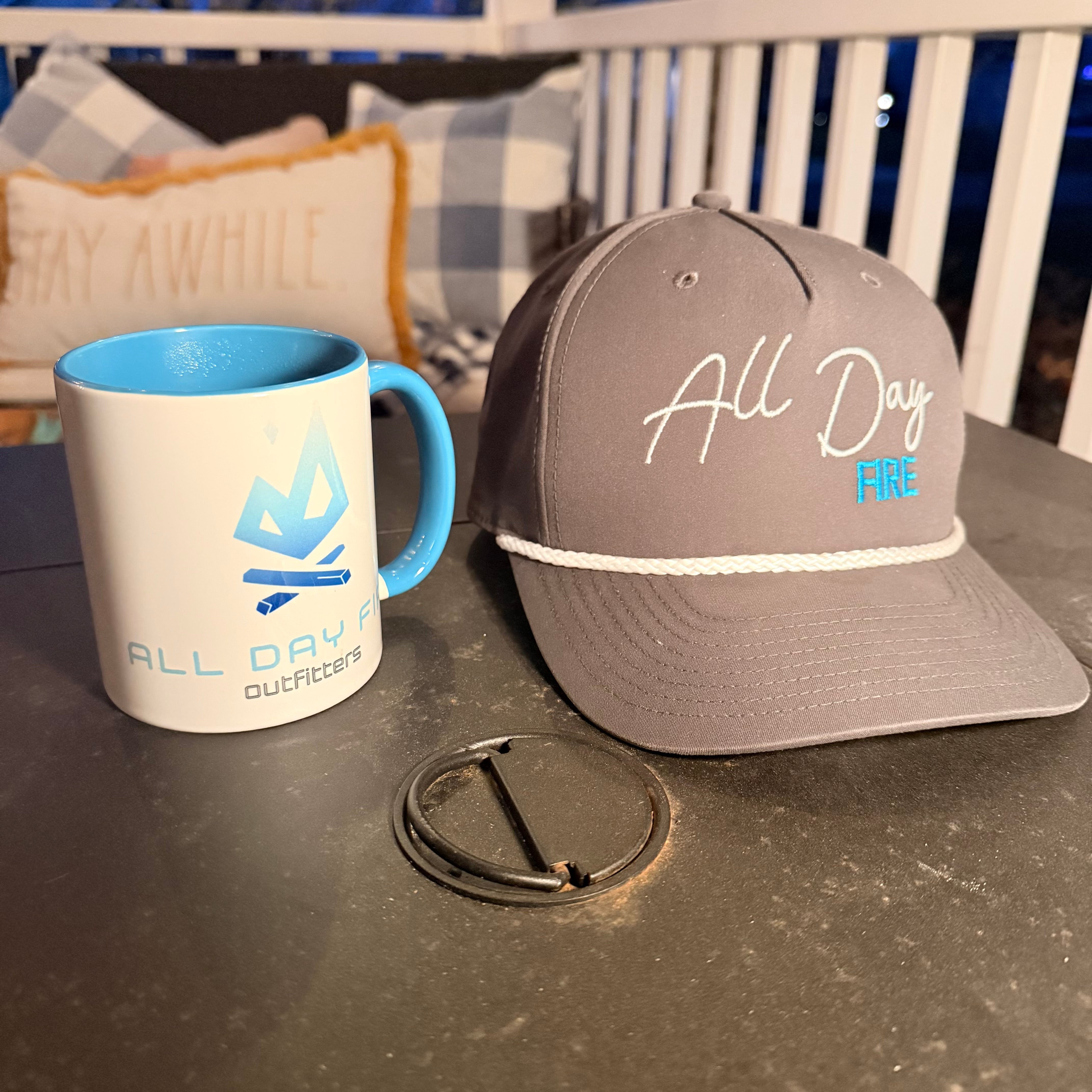 Stay Awhile Bundle with Richardson 168 All Day Fire hat and ceramic mug on outdoor table near fire pit.